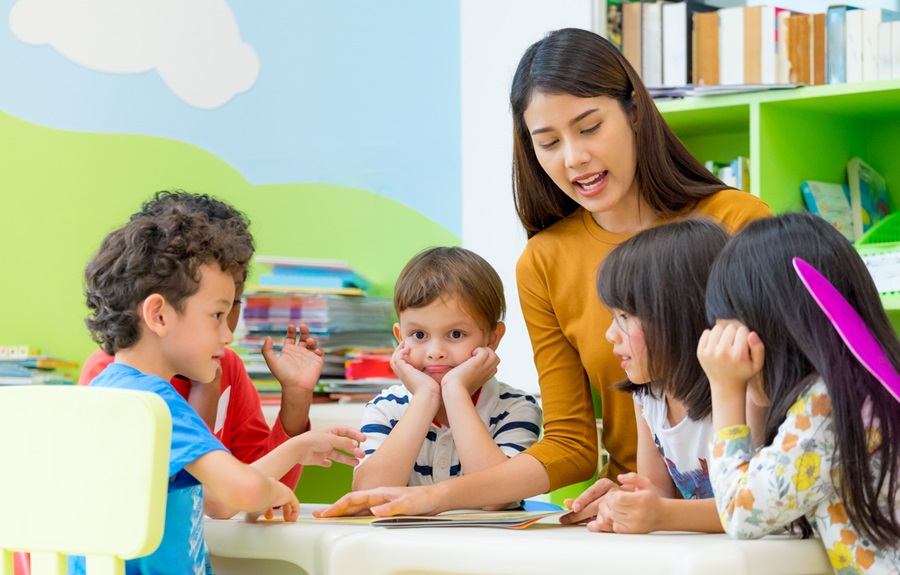 Asian female teacher teaching mixed race kids reading book in classroom,Kindergarten pre school concept.